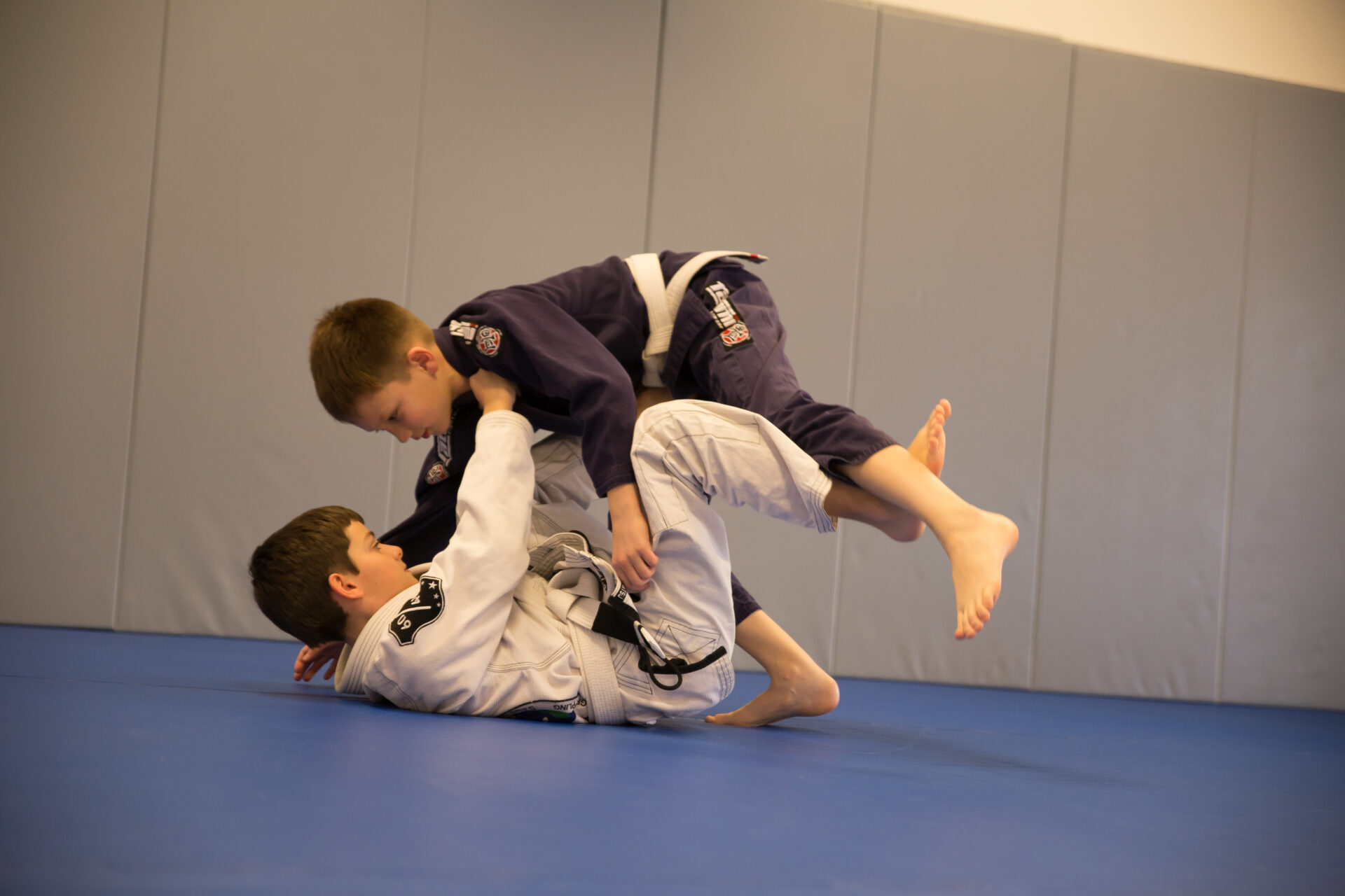 Two boys are practicing jiu jitsu on a blue mat.