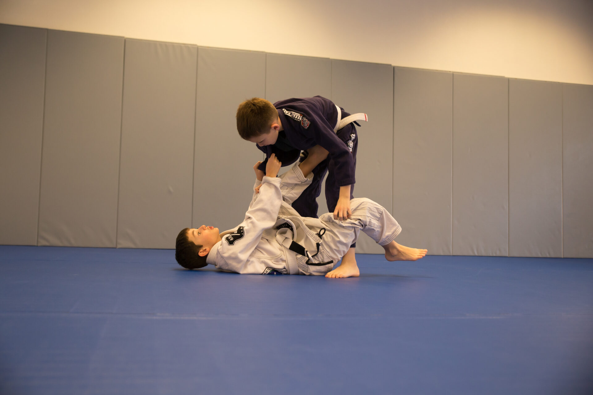 Two boys are practicing martial arts on a blue mat.